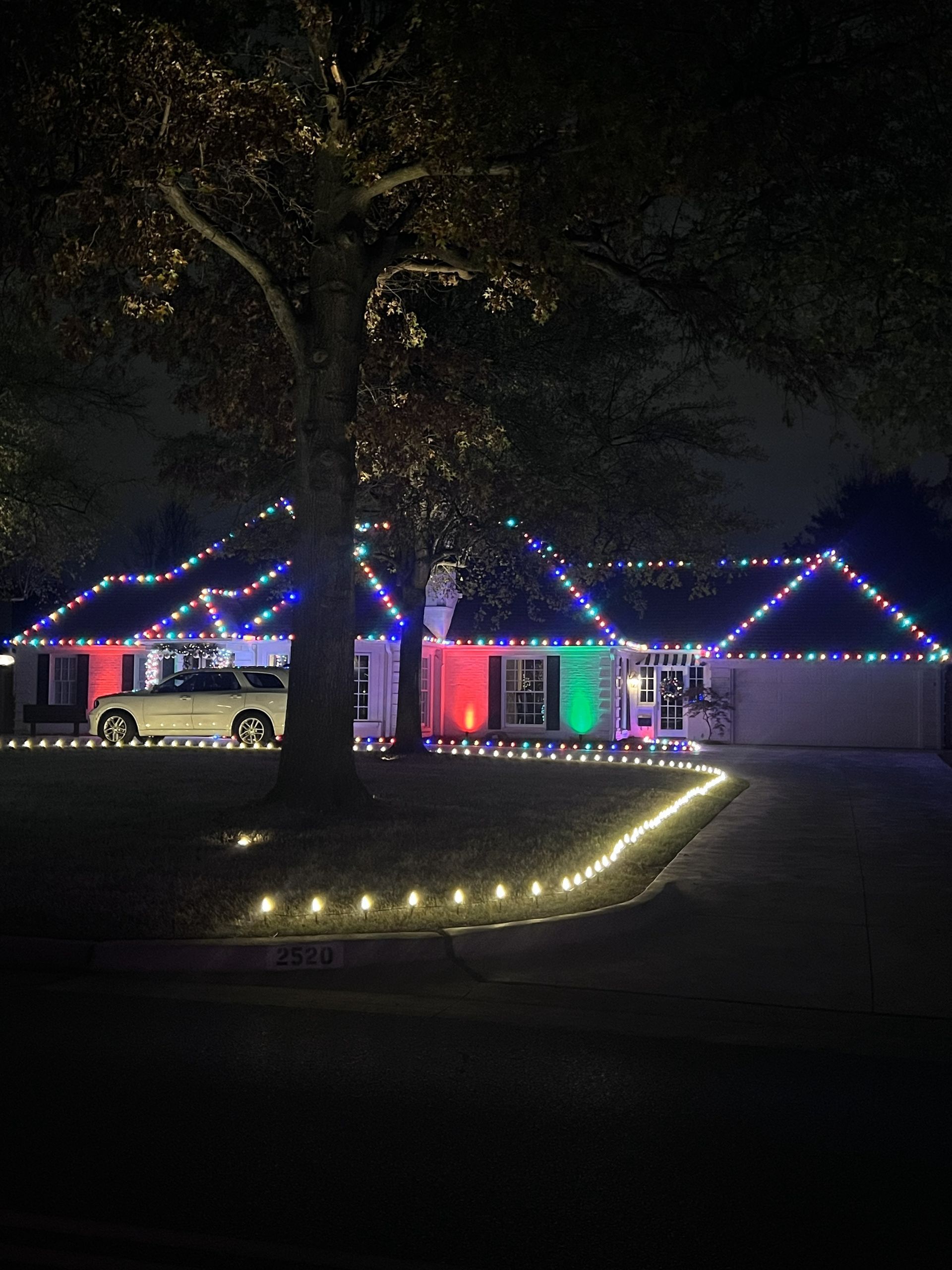 House decorated with colorful Christmas lights at night, a string of lights lines the driveway.