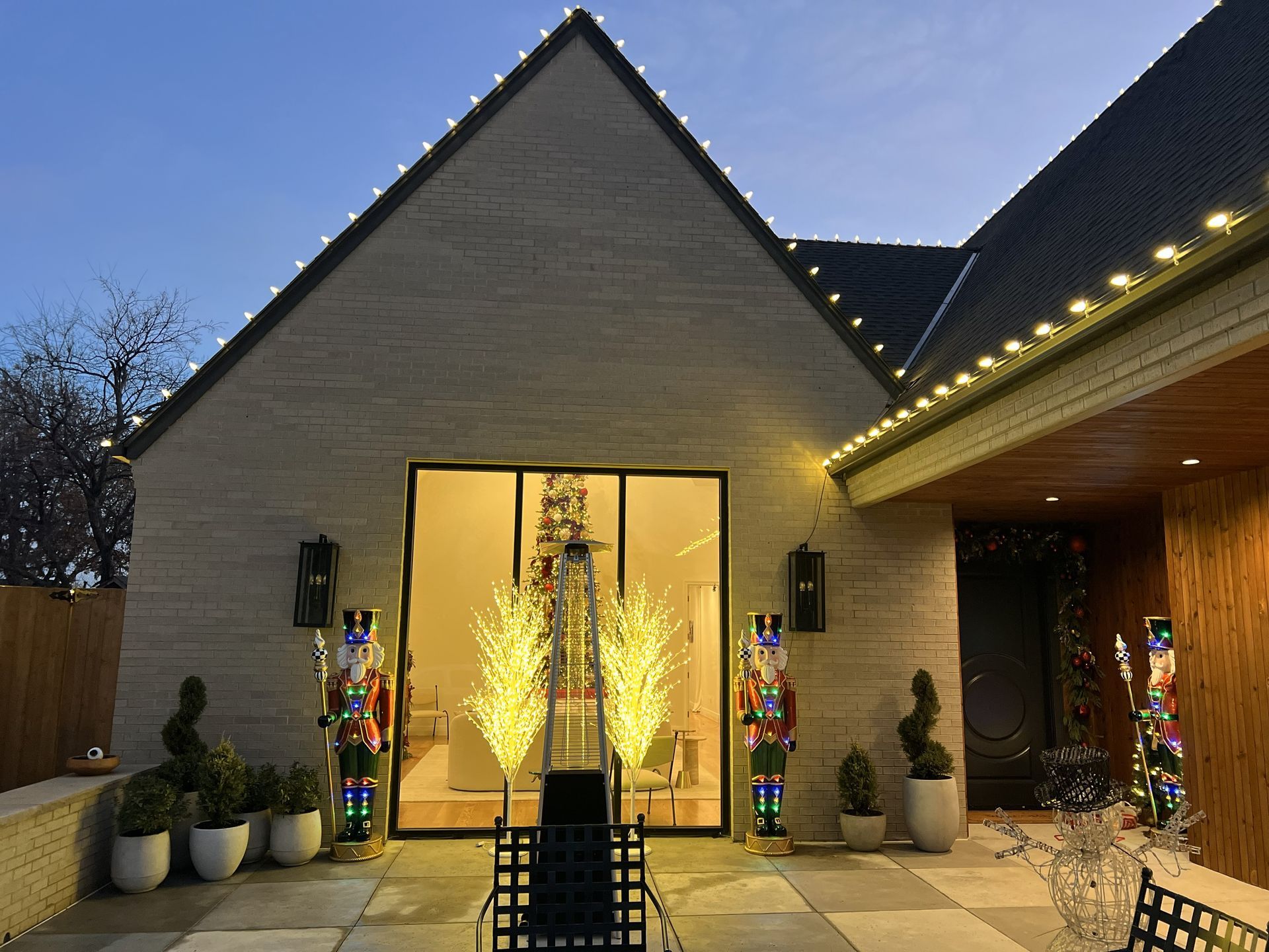 A house decorated for Christmas with lights on the roof, two nutcrackers, and lighted trees.