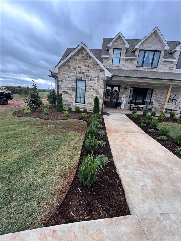 Stone-faced house with landscaped yard and walkway. Green lawn and cloudy sky.