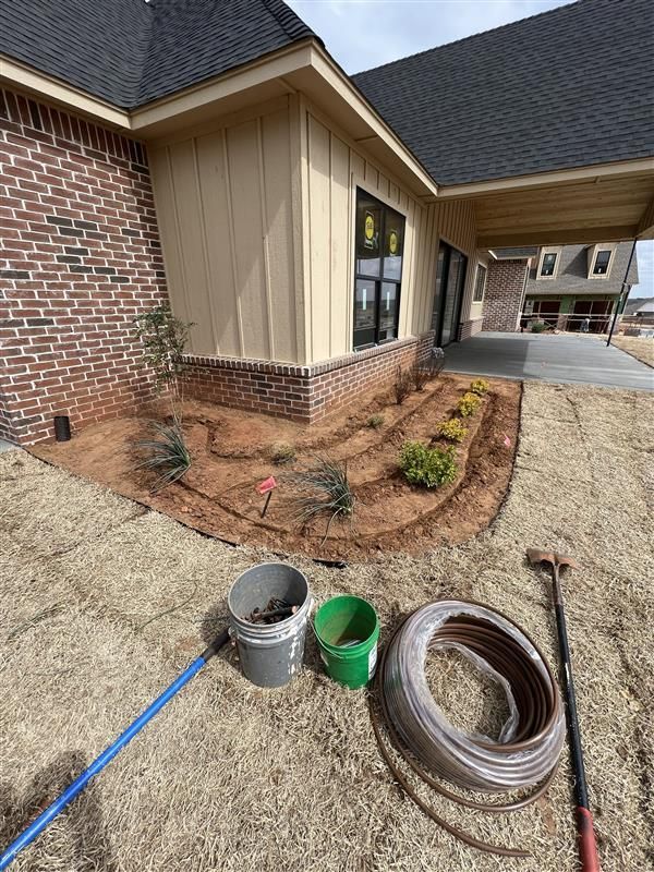 House exterior with newly planted garden bed and tools, next to an area of dried grass rolls.