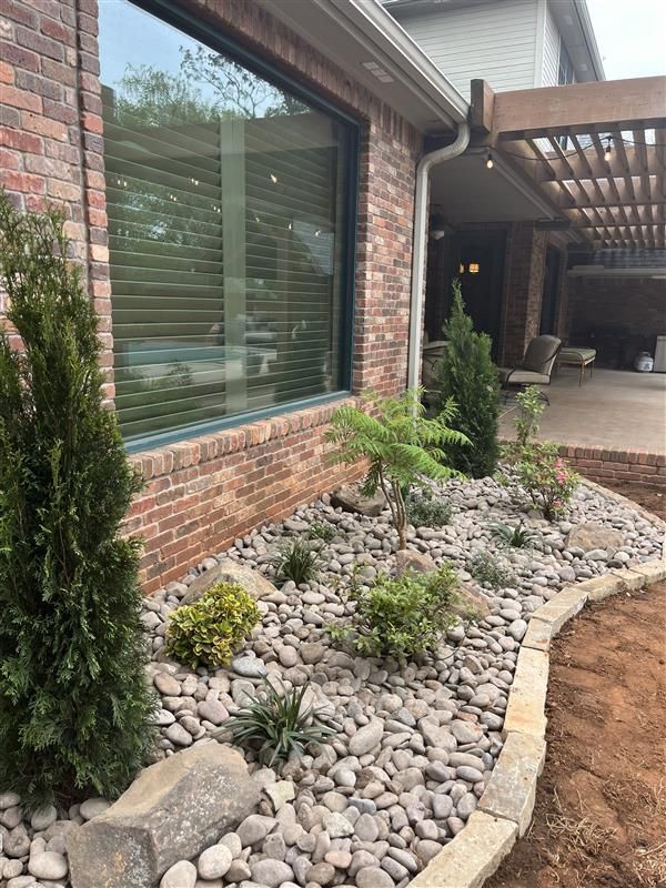 Landscaped garden bed with rocks, plants, and brick house exterior.