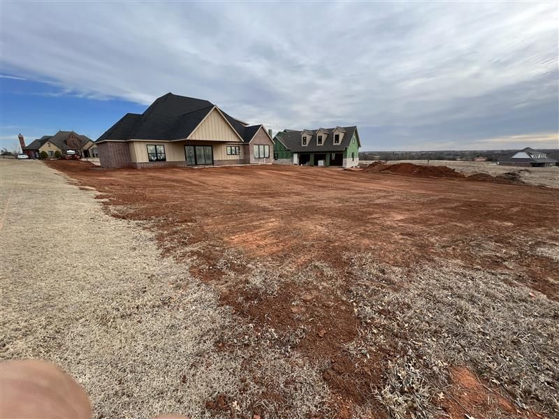 Houses under construction on a dirt lot; brown earth, gray gravel, blue sky.