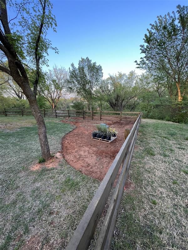 Backyard garden bed with fence, trees, and blue sky.