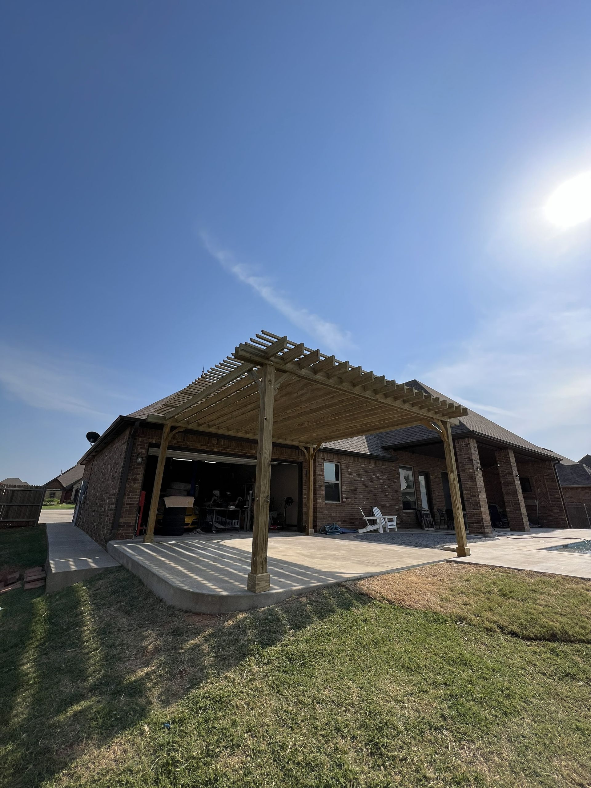 Pergola over a patio adjacent to a brick house on a sunny day.