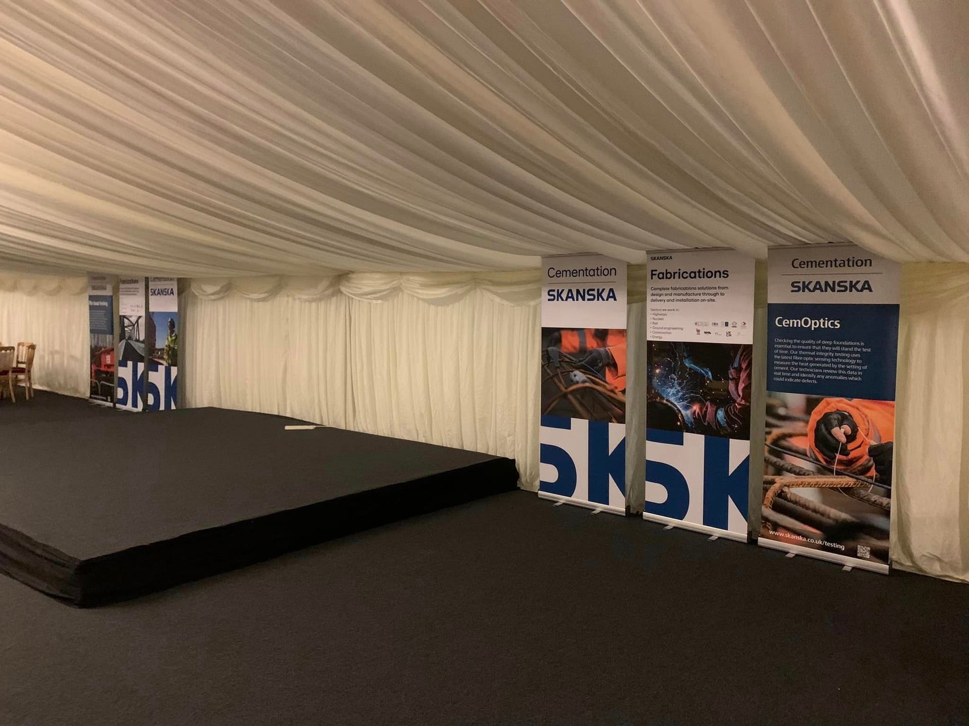 Marquee interior with stage and branded banners. Black carpet, white drapes, and banners promoting