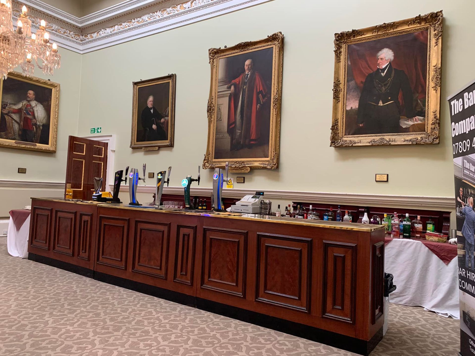 Long wooden bar in a room with portraits. Beer taps and bottles visible.