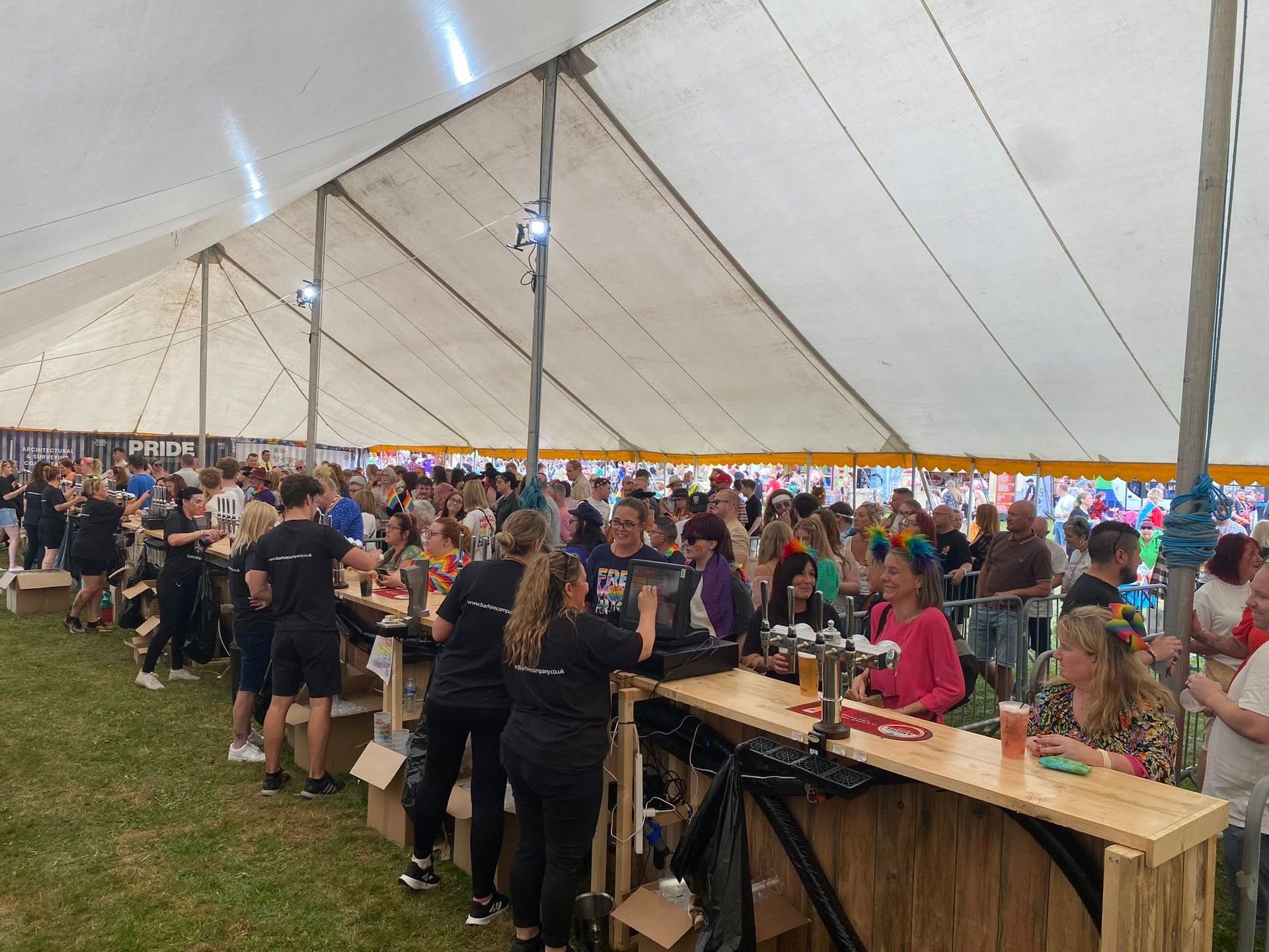 Large tent interior packed with people; a bar with staff serving drinks.