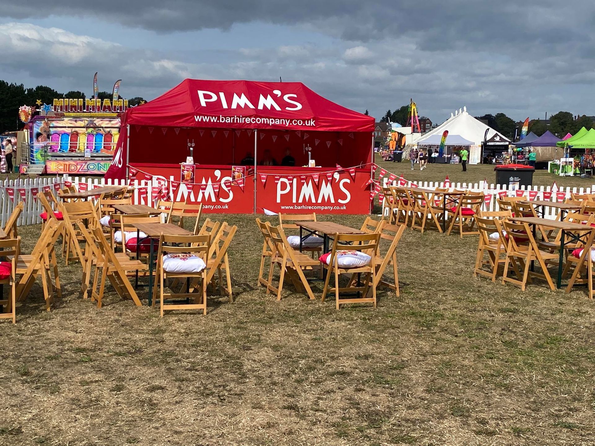 Red Pimm's bar tent at an outdoor event with tables and chairs set up on grass.