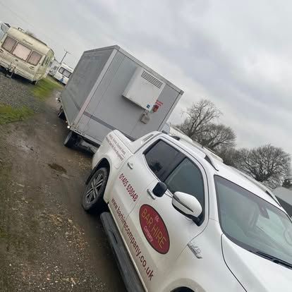 White pickup truck towing a large, refrigerated box trailer; a caravan is parked nearby.
