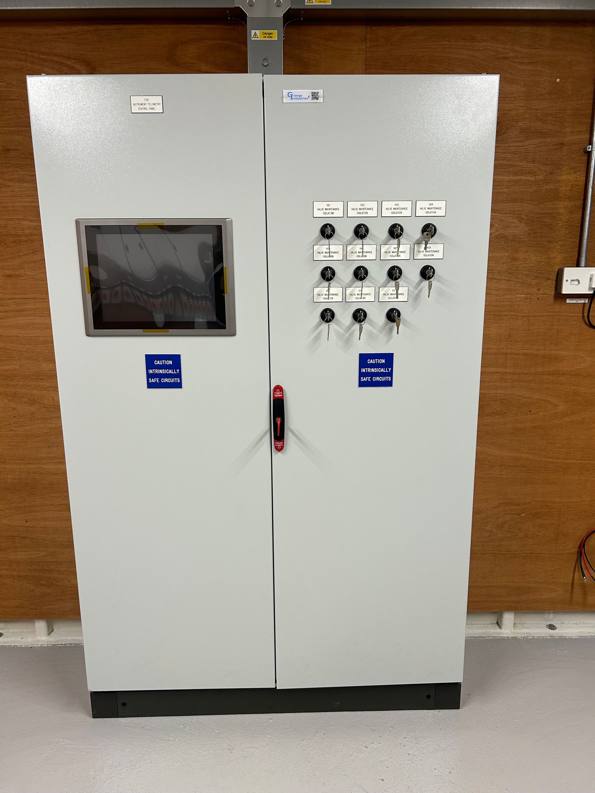 White electrical control cabinet with meter and switches against a wooden wall