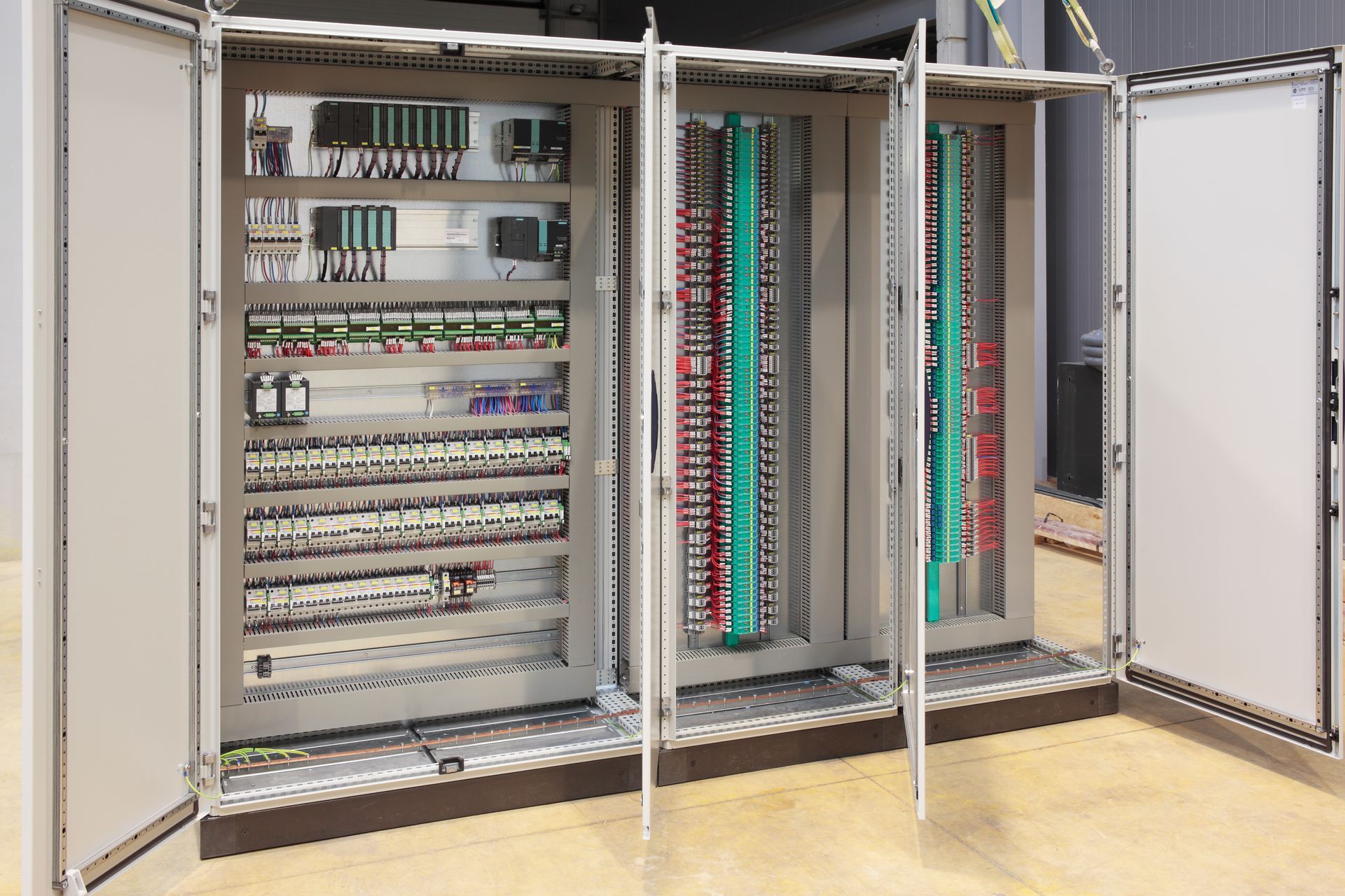 Open electrical control cabinet with rows of circuit breakers and wiring in a beige industrial setting