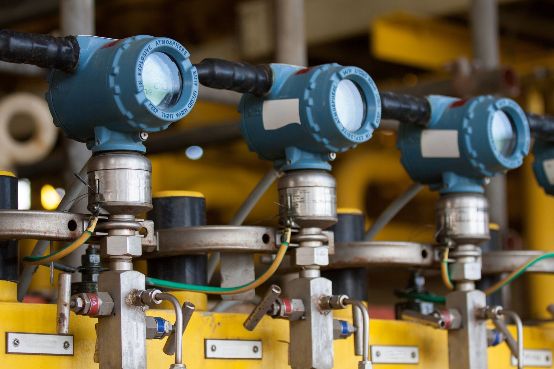 Blue industrial sensors mounted on yellow pipes in a factory setting