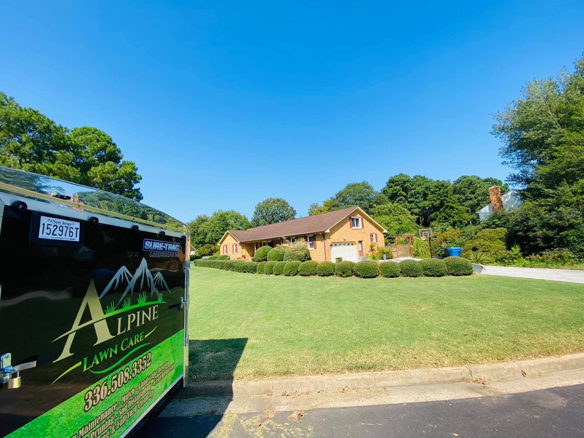 Lawn care truck parked on a street in front of a house with a well-maintained lawn and a blue sky overhead.