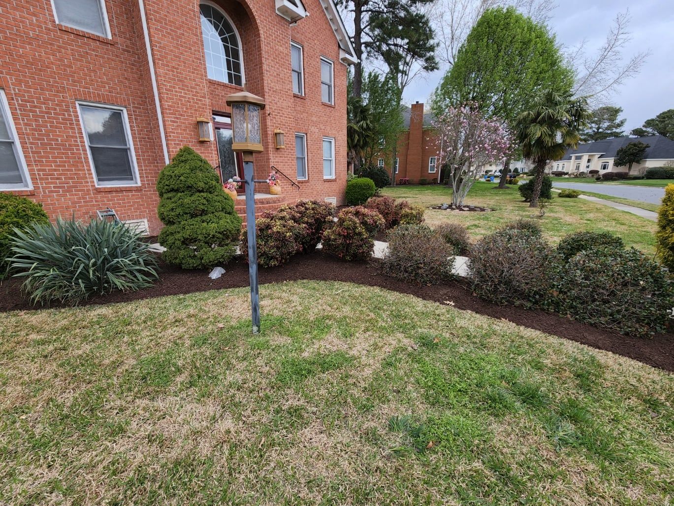 Red brick house with landscaped beds and a lawn; a bird feeder is in front.