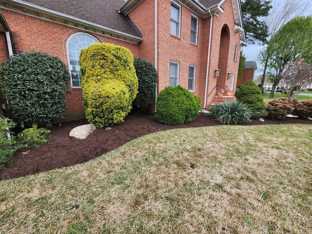 Brick house with landscaped bed, featuring shrubs, mulch, and lawn.