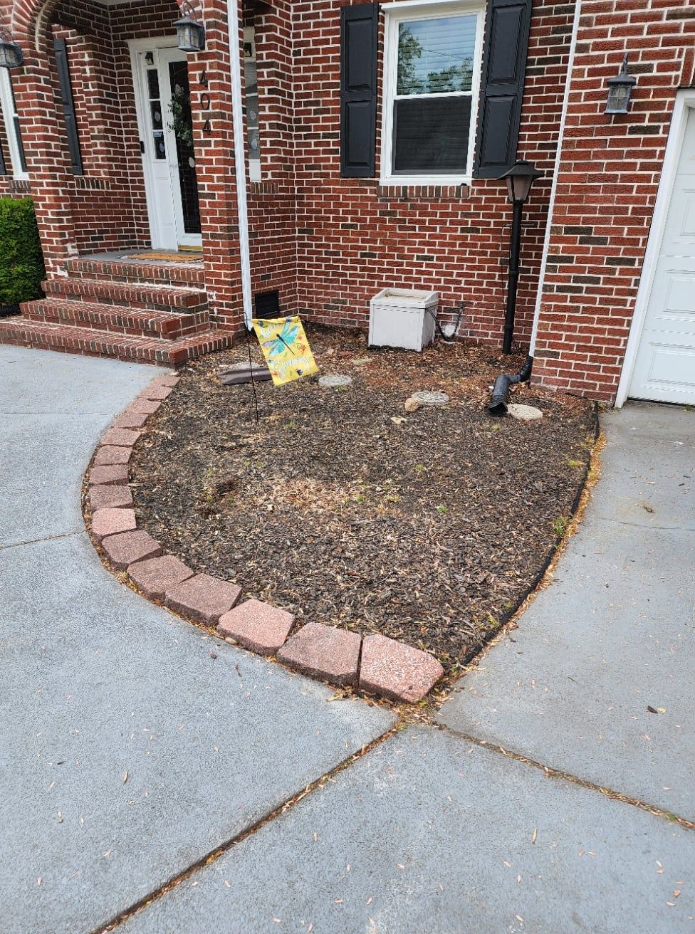 Brick house with a flower bed lined with bricks, filled with mulch.