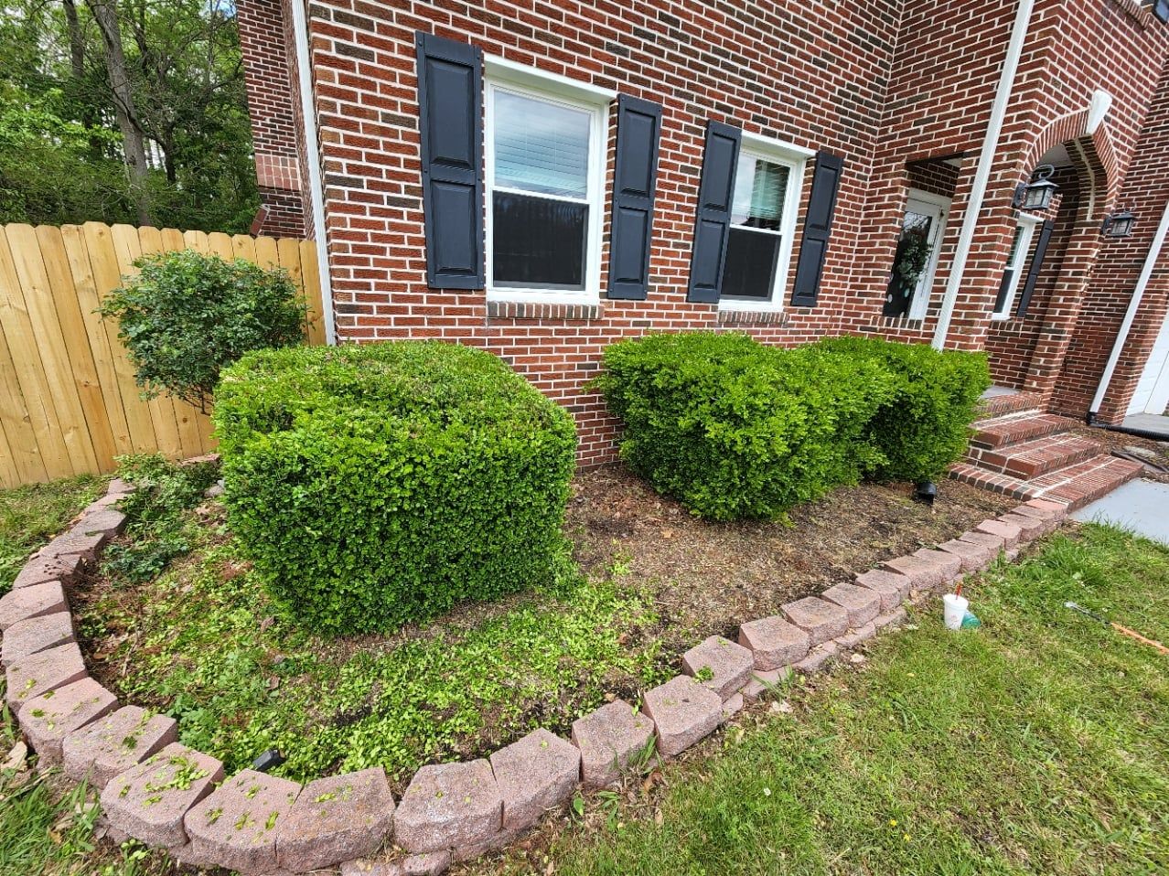 Red brick house with black shutters, green bushes, and a brick-bordered garden bed.