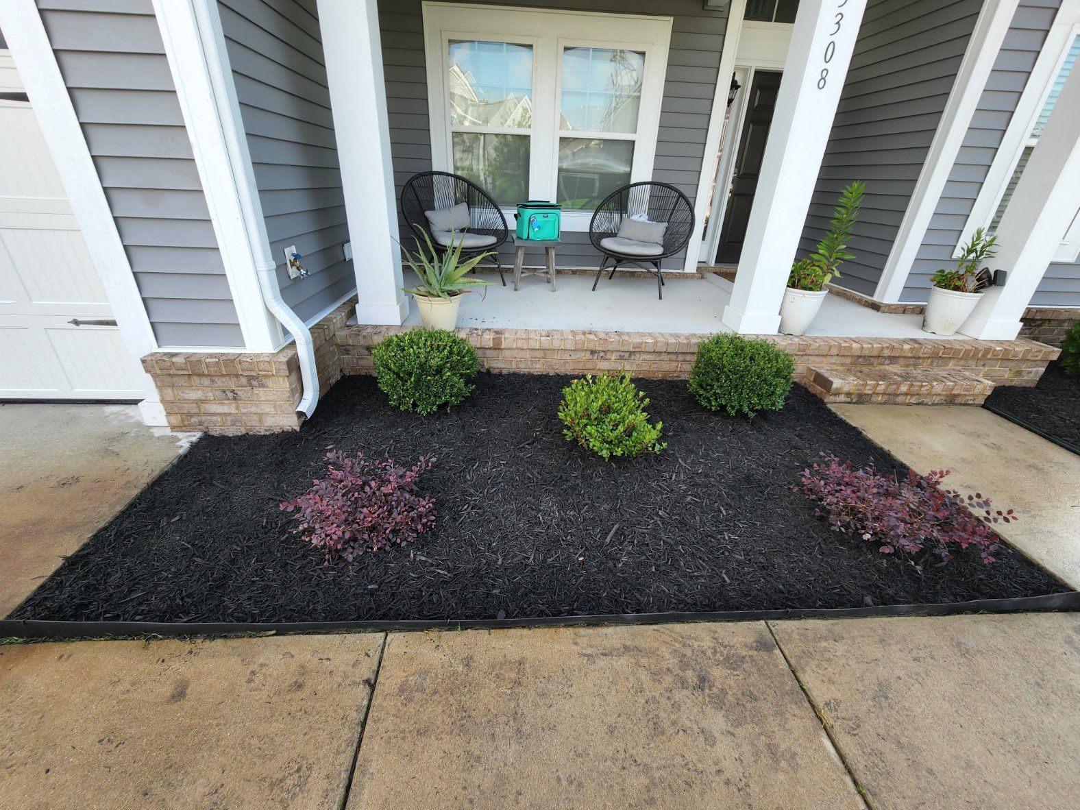 Front porch with gray siding, flower bed with black mulch, and shrubs.