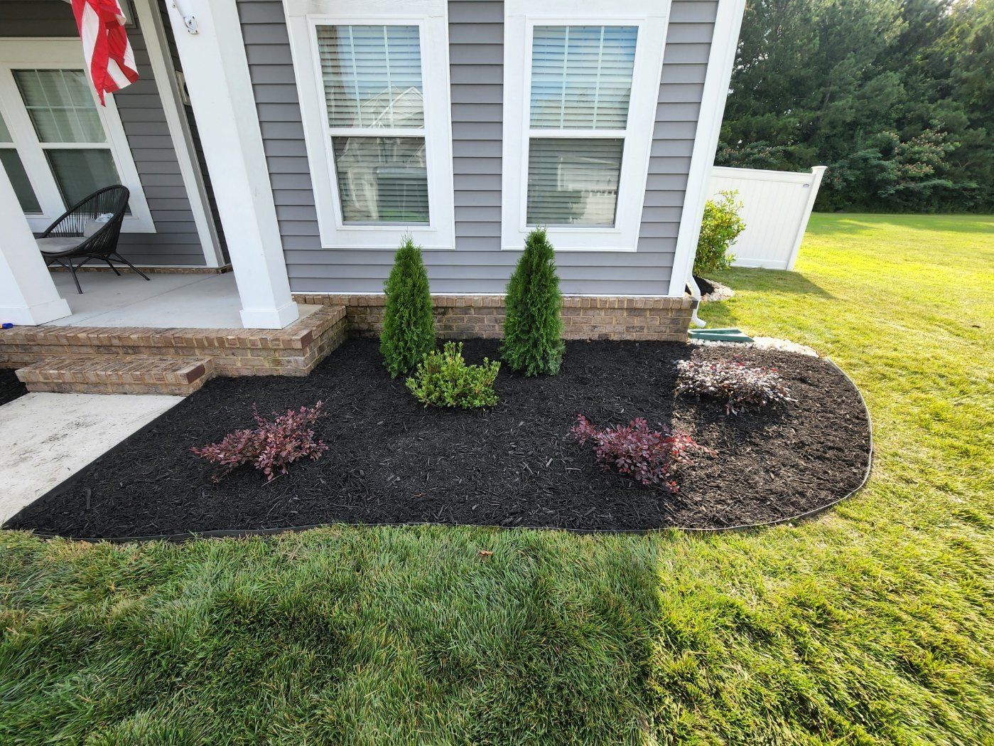 A landscaped front yard with dark mulch and green plants next to a house with gray siding.
