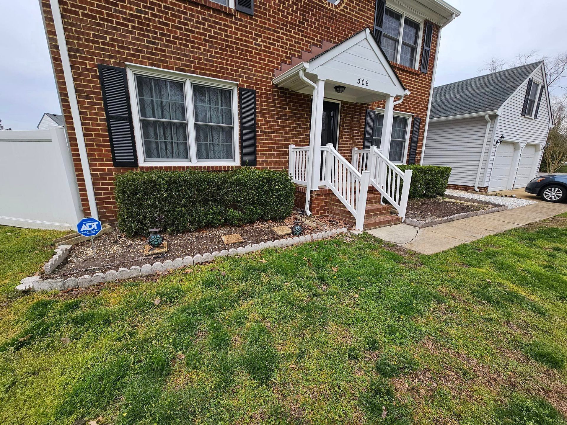 Brick house with a small porch, shrubs, and a lawn.