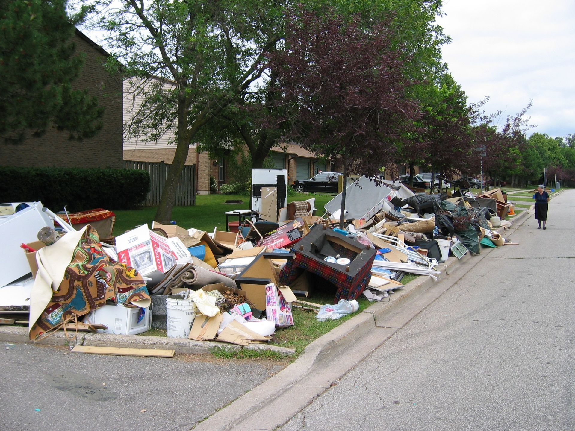 Pile of discarded household items on a curb, with a person walking on the sidewalk.