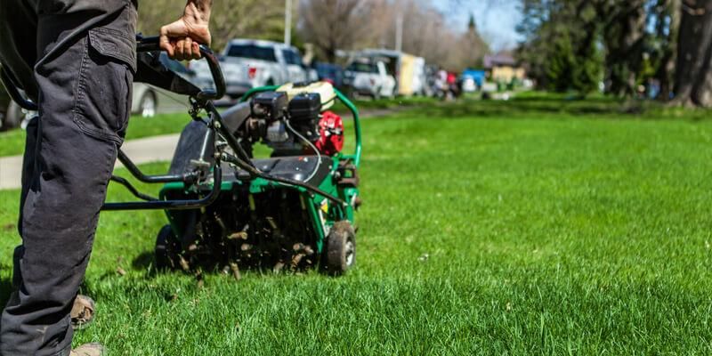 Person aerating a green lawn with a machine on a sunny day.