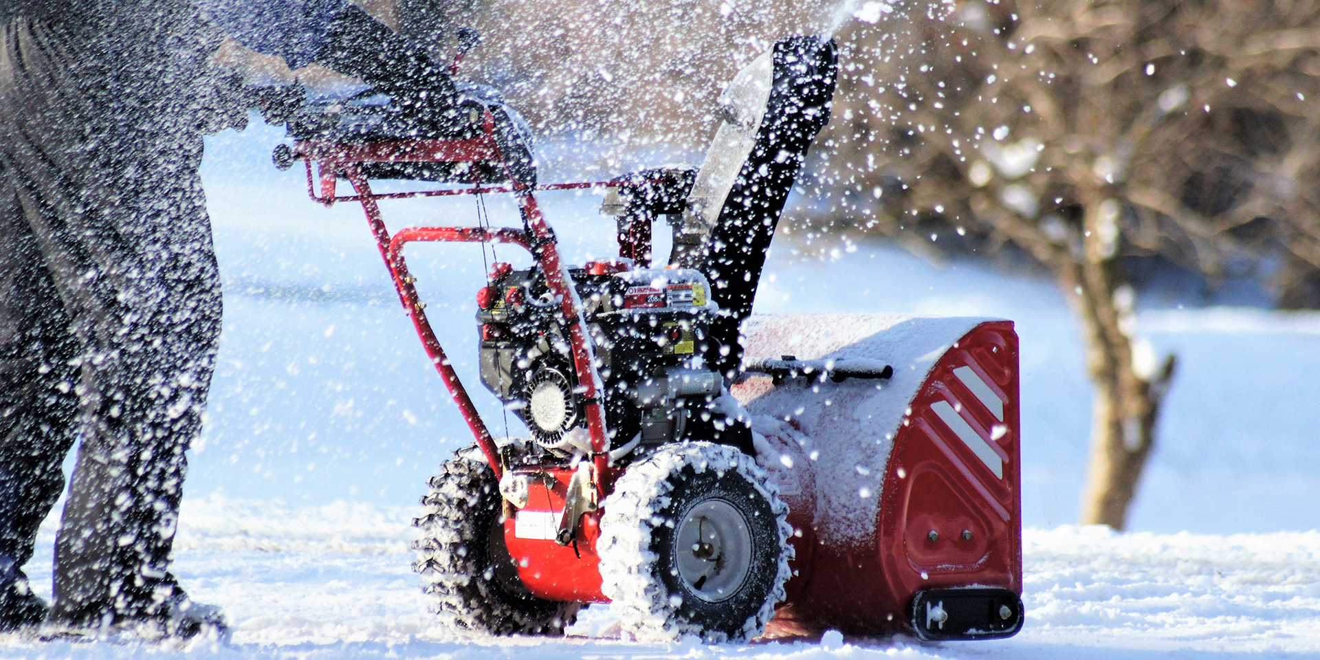 A person uses a red snowblower to clear snow.