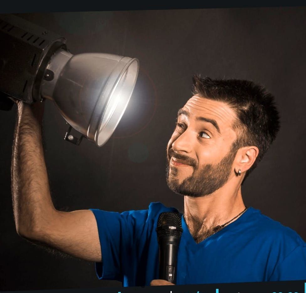 גבר מחזיק מיקרופון ומכוון פנס סטודיו כלפי מעלה, בחיוך, באולפן חשוך