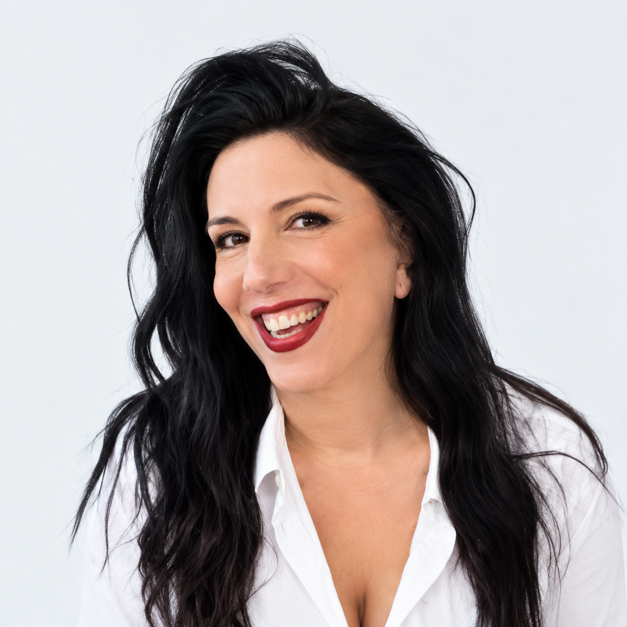 אישה מחייכת עם שיער שחור ארוך וחולצה לבנה על רקע בהיר
