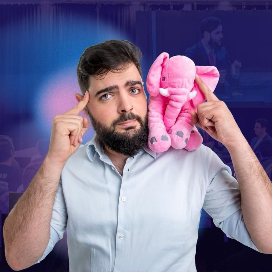 גבר מחזיק פיל ורוד ממולא ומצביע על הרקה שלו על רקע כחול־סגול