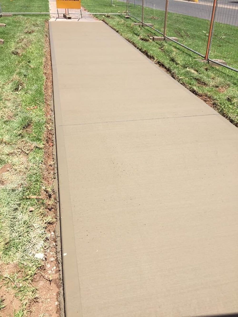 A Concrete Walkway Is Being Built Next To A Grassy Field — Heartland Concrete In Gillen, NT