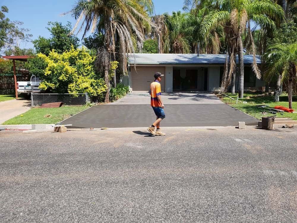 A Man Is Walking Down A Driveway In Front Of A House — Heartland Concrete In Gillen, NT