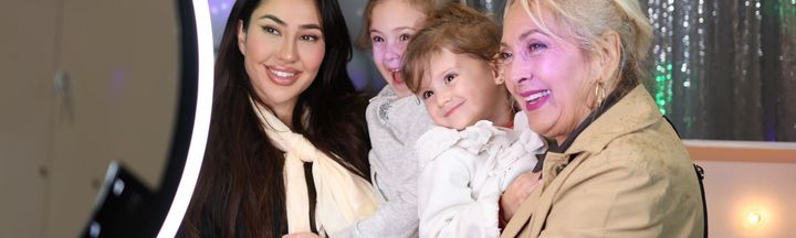 Three people smiling and posing together indoors, with one holding a small child.