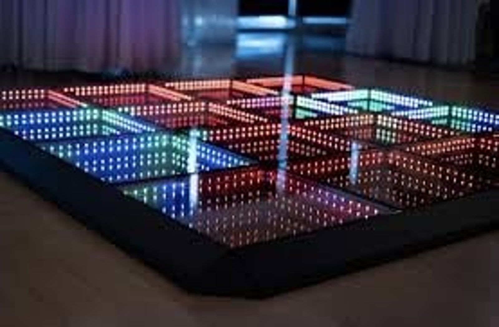 Colorful illuminated grid dance floor with reflective black surface in a dim room