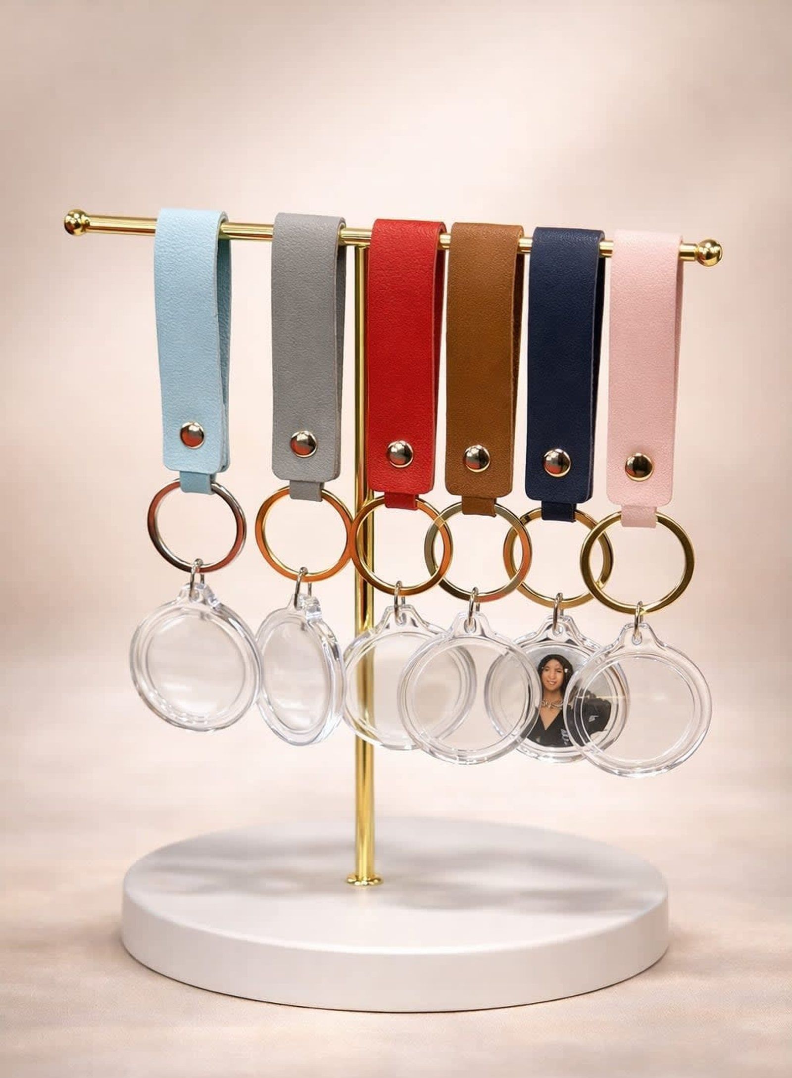 Five pastel wristlet keychains hanging on a gold stand with clear round tags on a white base