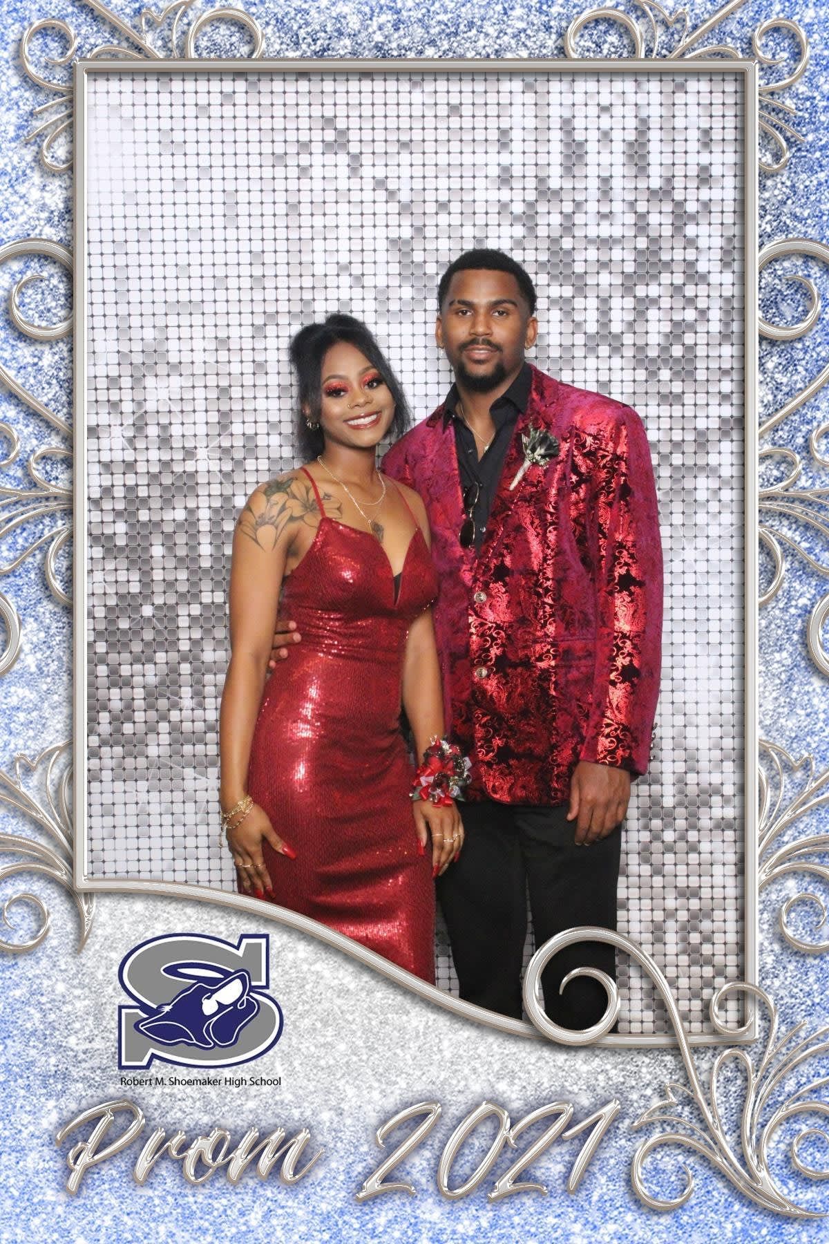 Couple posing in red outfits at Prom 2021 backdrop, smiling side by side