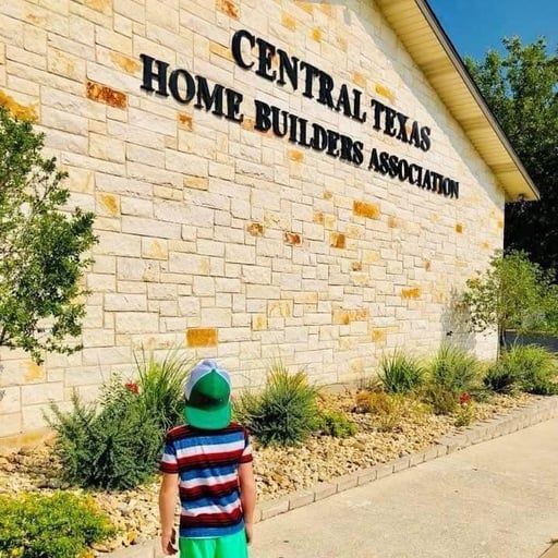 Child in striped shirt facing the Central Texas Home Builders Association stone sign outdoors