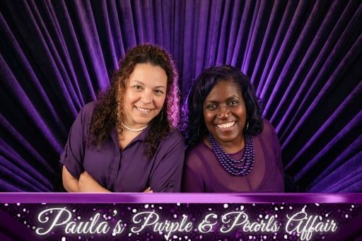 Two women in purple posing before a purple fan backdrop with “Paula’s Purple & Pink Affair” text