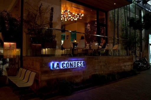 Exterior of La Condesa restaurant at night, with warm lighting and a blue neon sign.