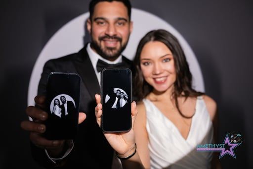 Two people smiling and holding smartphones in front of a dark backdrop with a circular logo.