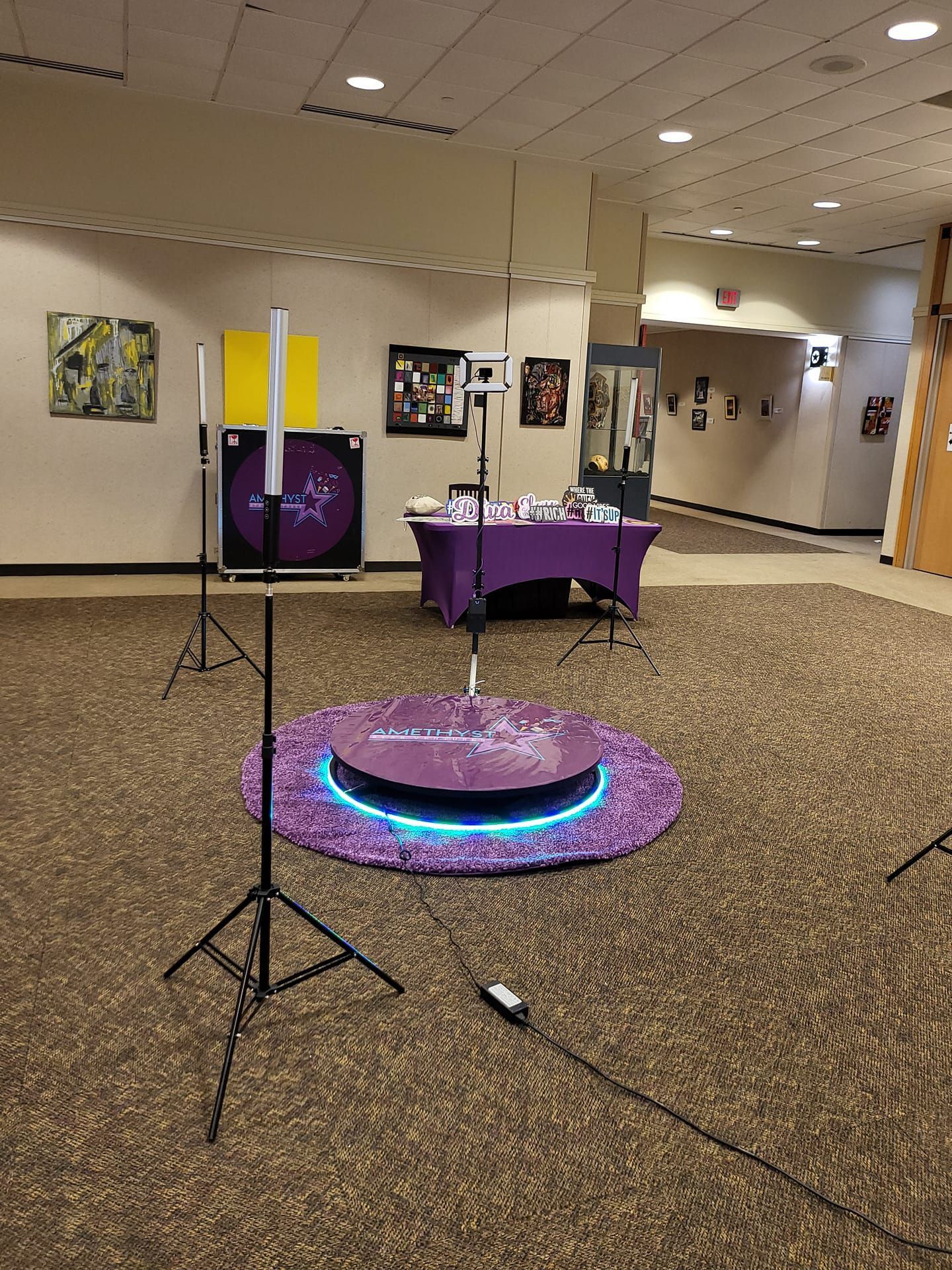 Event hall with a glowing LED floor platform and two black tripods in the foreground.