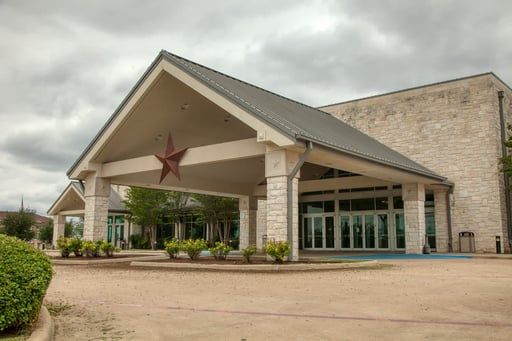 Covered entrance of a building with a red star, stone facade, and glass doors under a cloudy sky