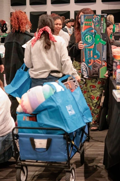 Crowded indoor market aisle with a blue shopping cart and colorful rolled rugs displayed on the right