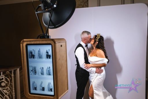 Bride and groom kissing during a wedding photo booth shoot with a vintage photo screen and studio backdrop