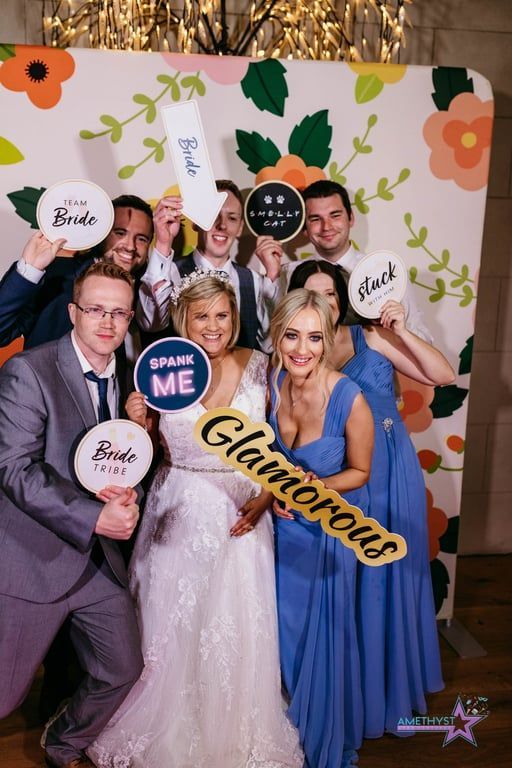 Five people in formal attire pose at a gala backdrop holding speech bubbles and a “Glamorous” sign.