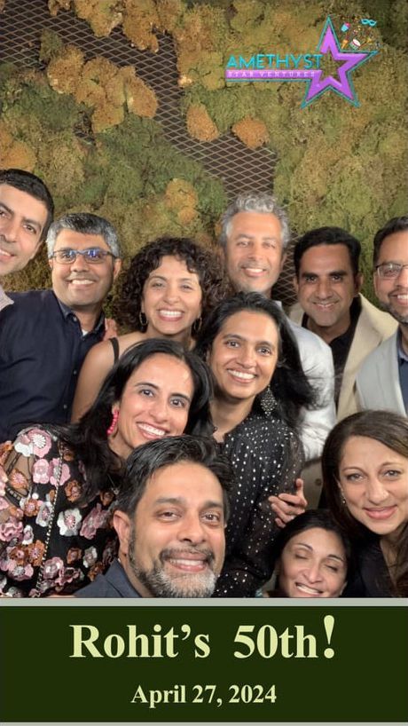 Group smiling at a birthday celebration banner reading “Rohit’s 50th!” with date April 27, 2024.