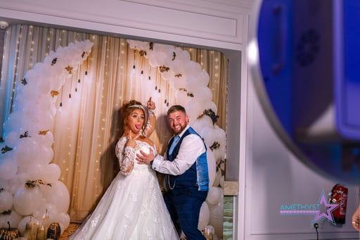 Couple posing in wedding attire before a cream floral backdrop