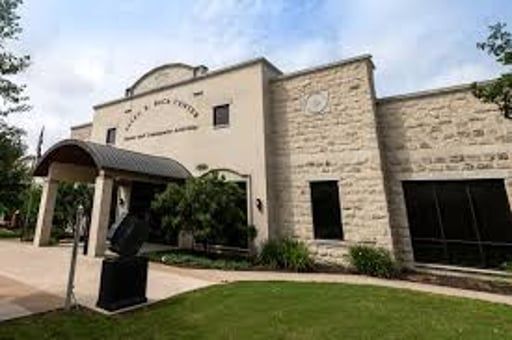 Stone building entrance with arched awning, landscaped lawn, and blue sky