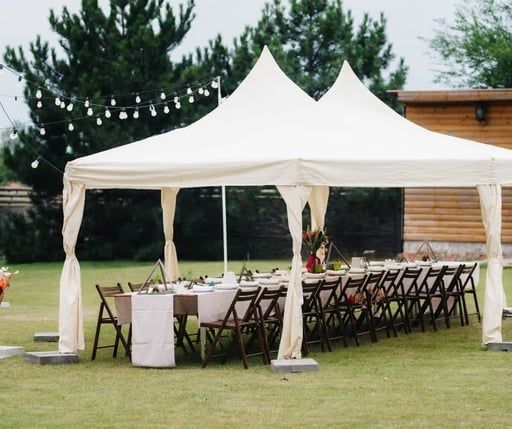 White outdoor event tent with tables and folding chairs on a grassy lawn