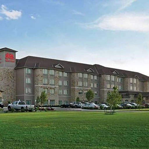Four-story hotel with a green lawn and parked cars under a blue sky